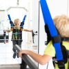 Chłopiec w uprzęży OSTIUM ćwiczący chód przy poręczach rehabilitacyjnych.