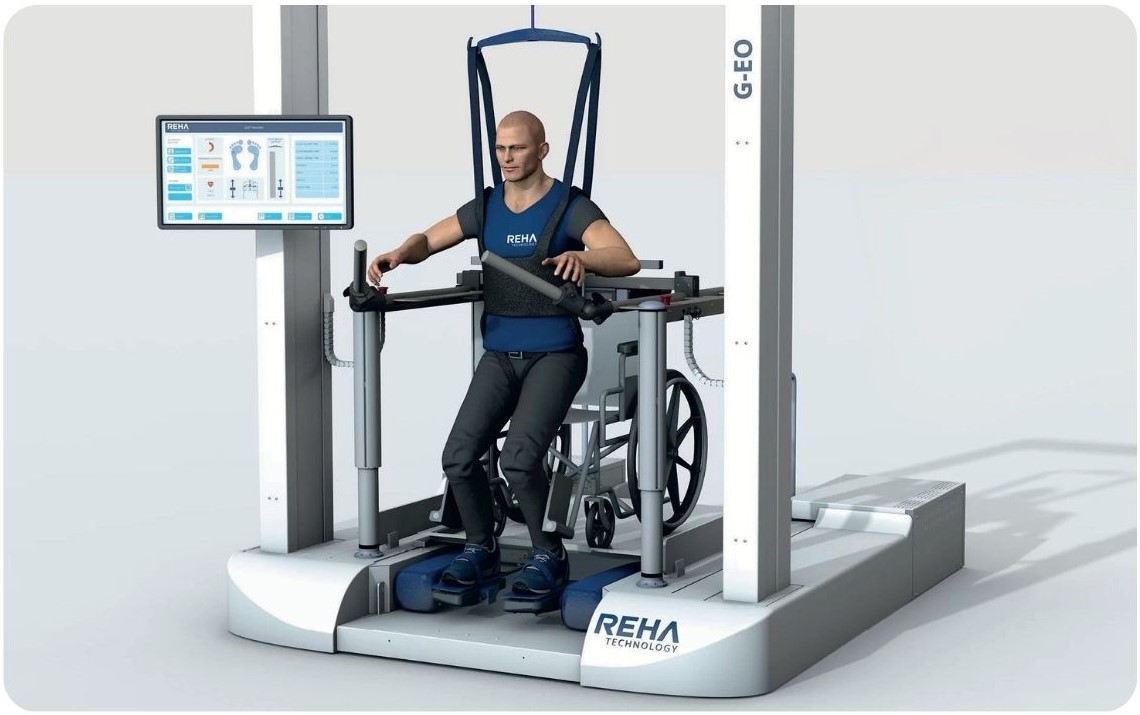 Stanowisko systemu G-EO z pacjentem podczas treningu chodu, z widocznym panelem sterowania i podestami pod stopami.